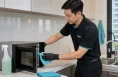 KleanSG cleaner wiping a microwave and kitchen surface during home cleaning in Singapore
